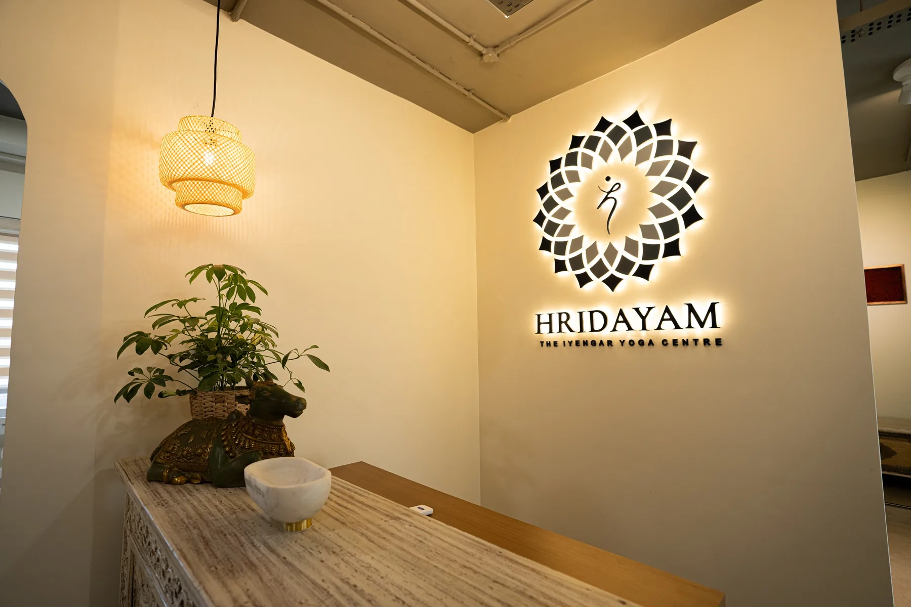 The Hridayam sign at the entrance: the mark and name on a cream wall, lit from behind