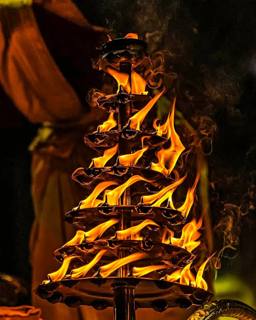 A tiered brass lamp alight during an evening aarti