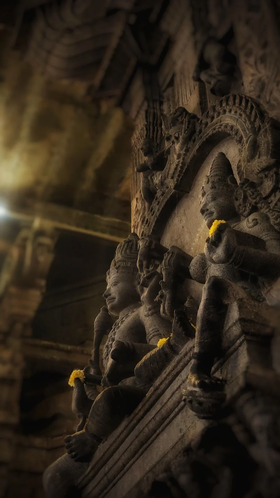 Carved stone figures in a dim temple hall, each holding a fresh marigold